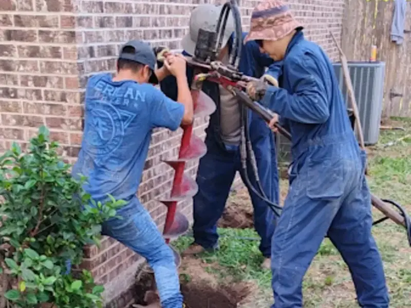 Action House Leveling crew drilling a foundation pier hole next to a brick home in the Rio Grande Valley