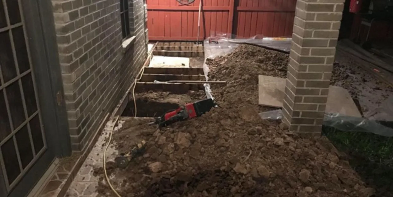 Excavated foundation pit with jackhammer next to RGV brick home during reinforced concrete pier repair