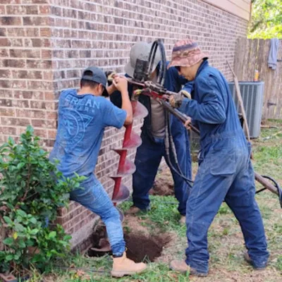 Action House Leveling crew drilling a foundation pier hole next to a brick home in the Rio Grande Valley
